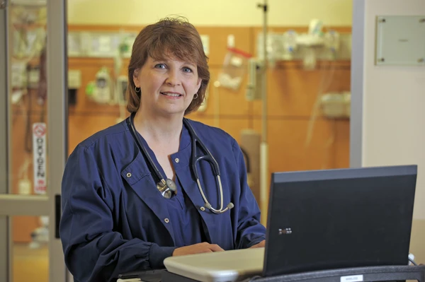Woman in nursing scrubs at a laptop.