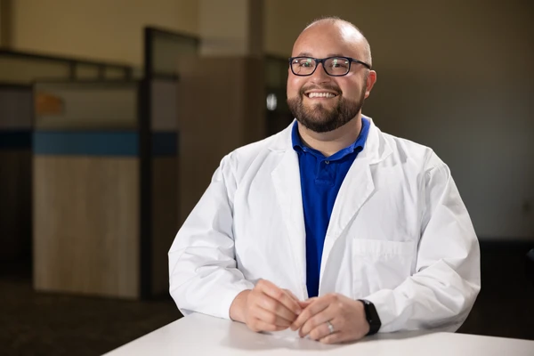student in labcoat smiles for a photo in an office setting