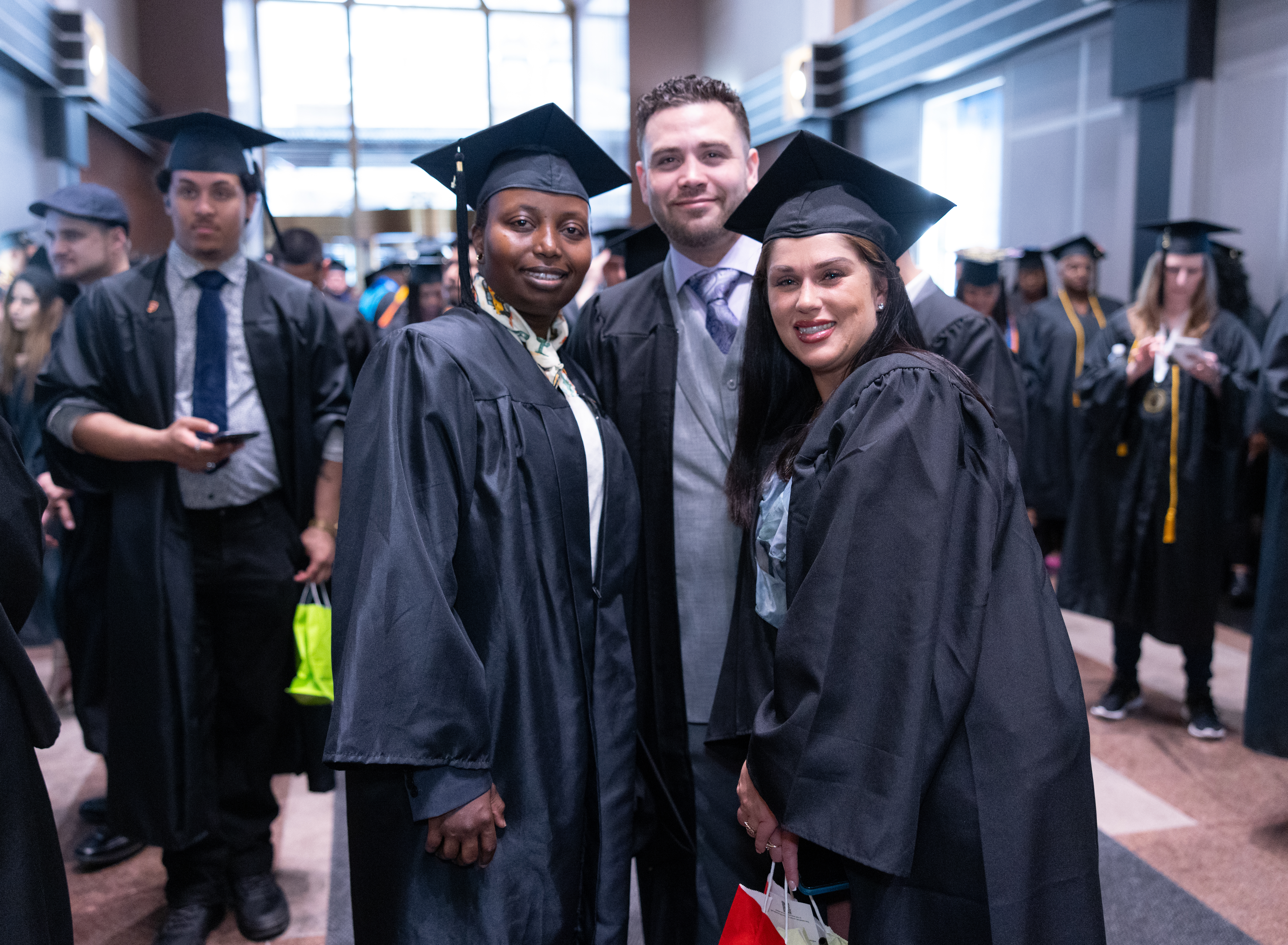 3 smiling students in caps and gowns pose for a photo